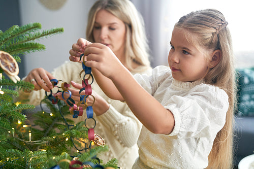 Caucasian little girl and mother decorating Christmas tree with DIY paper chain