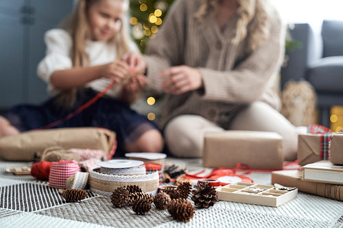 Christmas decorations on foreground and girl and mother wrapping Christmas gifts on floor in the background