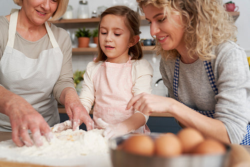 Little girl with her mom and grandma kneading dough together