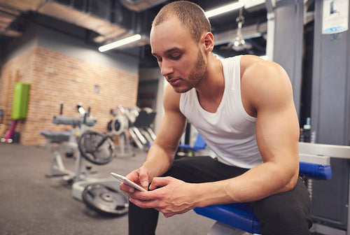 Muscular young man using cell phone at gym