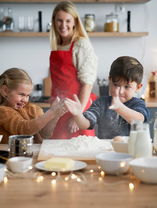 Vertical image of children clasping using flour while baking cookies