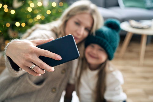 Caucasian mother and daughter taking selfie with smart phone with Christmas tree in the background