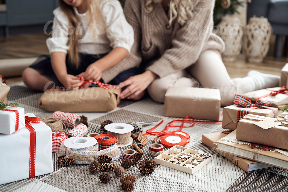 Christmas decorations on foreground and girl and mother wrapping Christmas gifts on floor in the background 