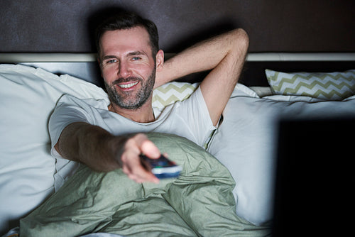 Man lying on the bed and watching tv at night
