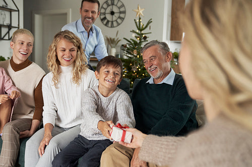 Caucasian boy giving Christmas present to his mom and family sitting around