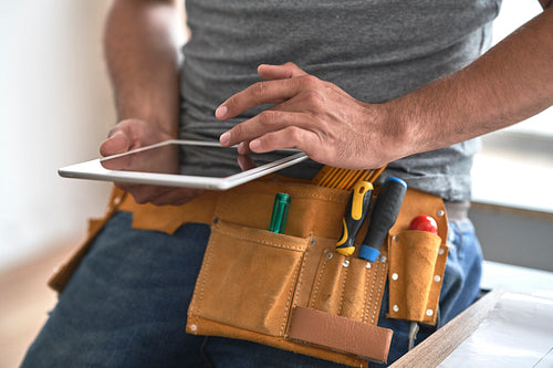 Close up of carpenter with tool belt scrolling digital tablet