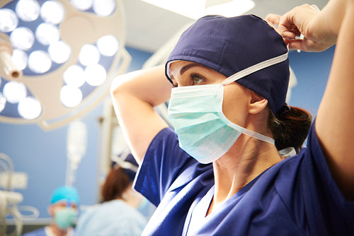 Side view of young female surgeon tying her surgical mask
