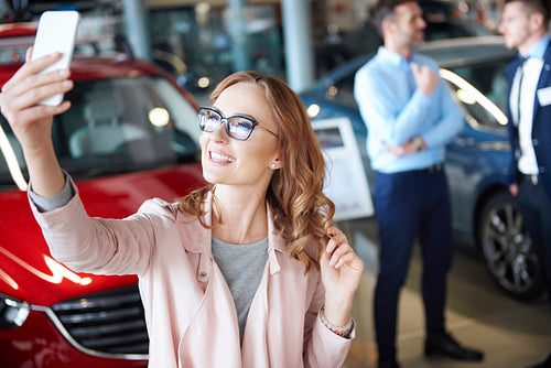 Young woman taking picture in the car dealership