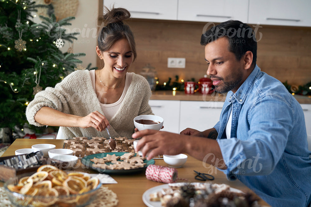 Multi ethnicity couple decorating sweet cookies at home during the Christmas 