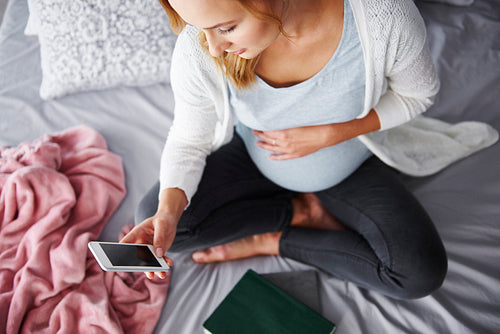 Pregnant woman using mobile phone at bedroom