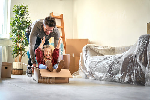 Caucasian father pushing little girl in paper box while moving house