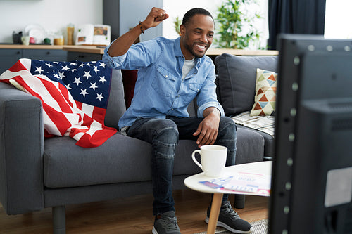 Wide image of black man cheering in front of TV