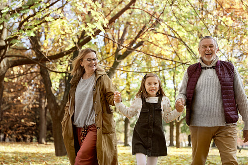 Senior couple with granddaughter walking at the park during the autumn