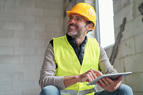 Caucasian engineer sitting on stairs and browsing digital tablet on construction site