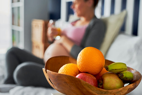 Pregnant woman and bowl of fruits in the foreground