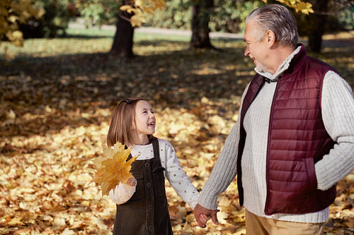 Little girl spending time with grandfather at the park in autumn