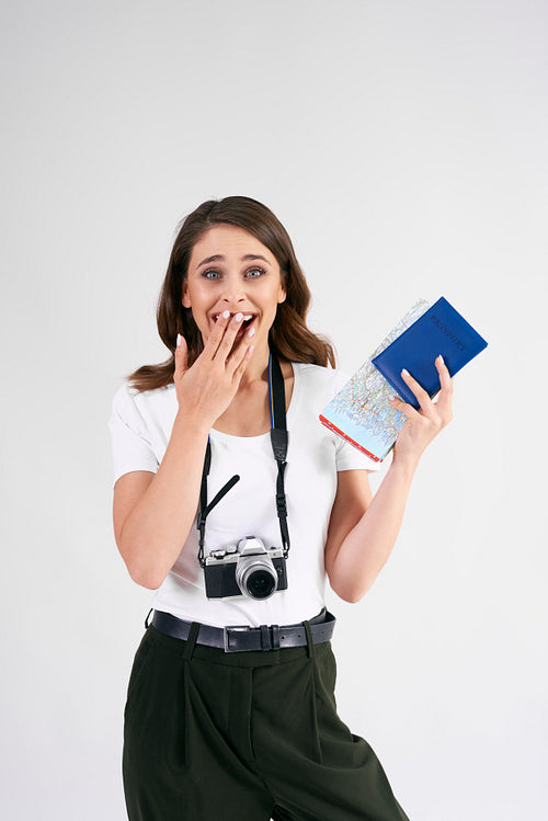 Surprised tourist with camera, map and passport in studio shot