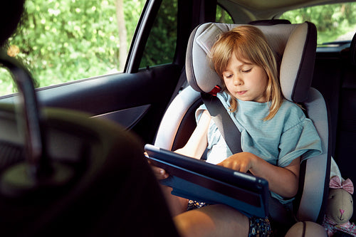 Little girl using digital tablet on rear seat of car