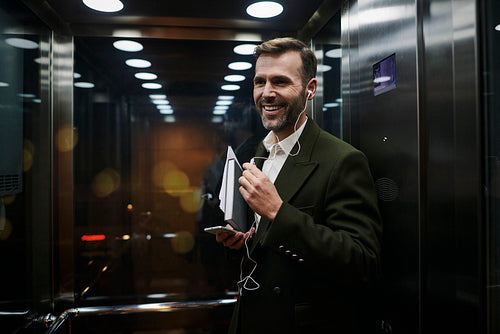 Portrait of smiling businessman listening to music in elevator