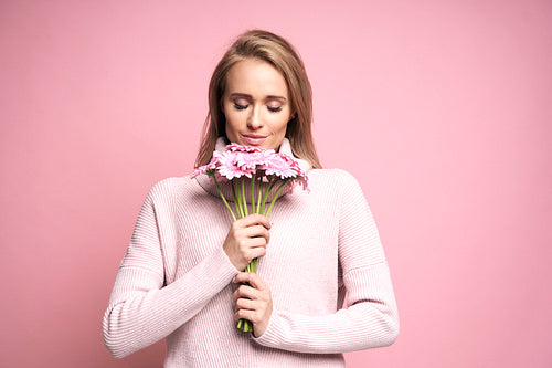 Studio shot of caucasian young woman smelling a bunch of flowers