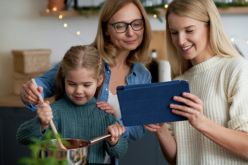 Three generations of women in the kitchen cooking with a tablet
