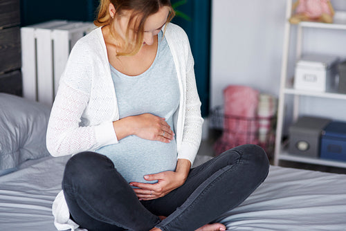 Affectionate pregnant woman touching her belly at home