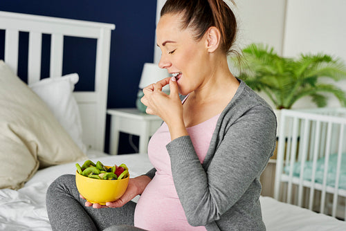Cheerful pregnant woman eating a bowl of fruits