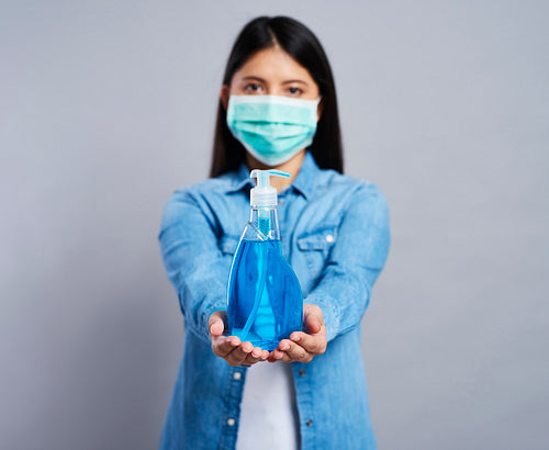 Woman in surgical mask holding a cleaning product