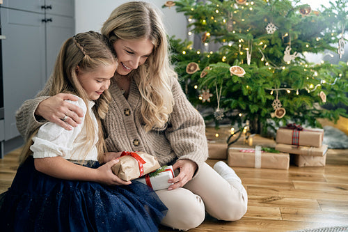 Caucasian girl and mother embracing each other and holding Christmas gift