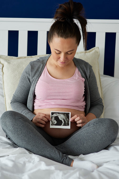 Pregnant woman holding ultrasound image on her abdomen