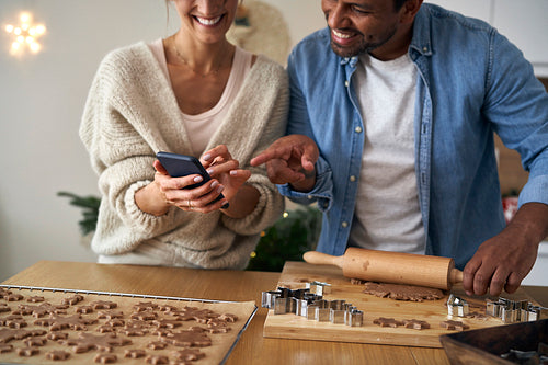Close up of multi ethnicity couple making a gingerbreads and using mobile phone in Christmas time