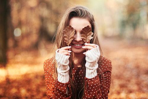 Woman covering eyes with autumnal leaves