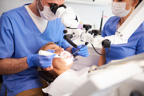 Dentist using dental microscope and examining woman's teeth