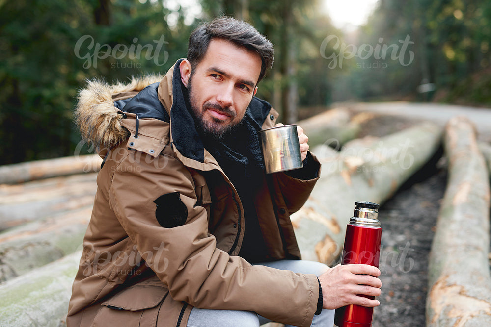 Portrait of handsome man drinking hot tea in autumn forest