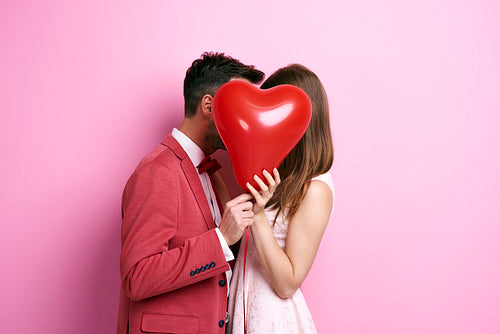Affectionate couple covering face with balloon and kissing