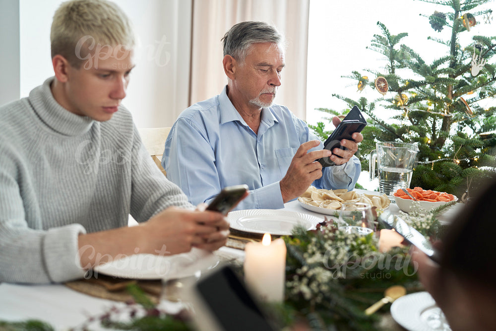 Caucasian young man and senior spending Christmas Eve with mobile phone