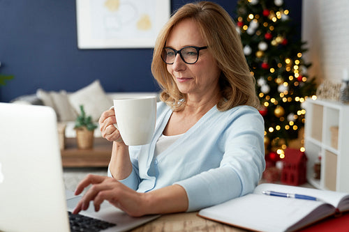 Mature woman drinking coffee in front of laptop