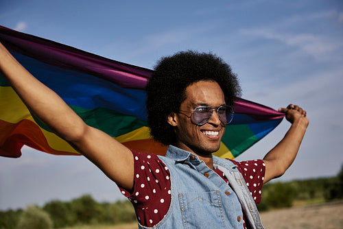 Young African man with rainbow flag standing at beach