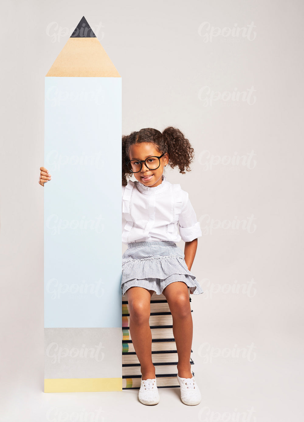 African girl sitting on books and holding big pencil