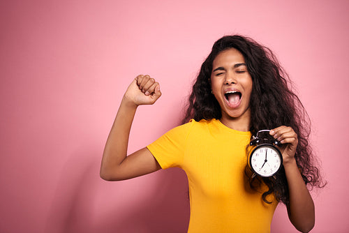 African woman holding an alarm clock and yawning.