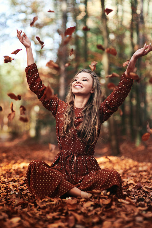 Beautiful young woman throwing leaves in the autumn forest