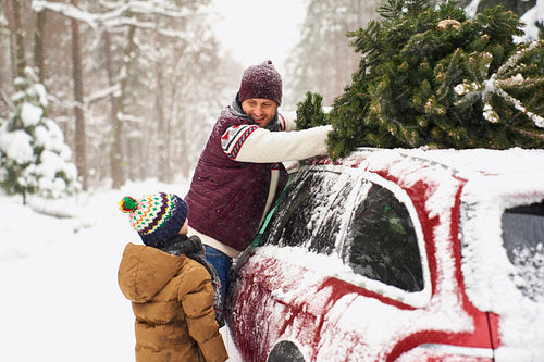 Man with son loading Christmas tree into roof of car