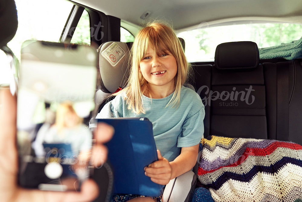 Little girl in car with tablet smiling for the picture