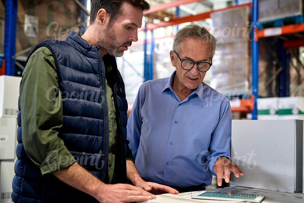 Two caucasian men in mature age discussing over digital tablet in warehouse 
