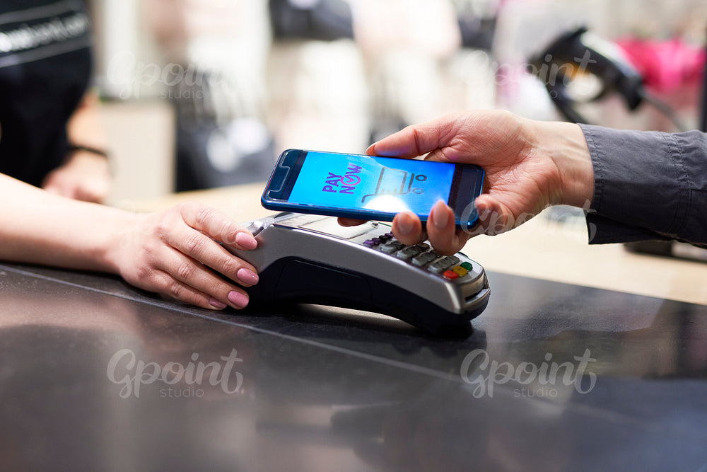 Woman's hand with mobile phone paying at checkout