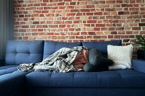 Woman with emotional problems lying on the couch and covered with a blanket