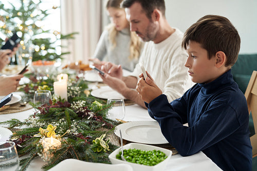 Boy in the foreground and family in the background sitting in silence and using phones during Christmas Eve