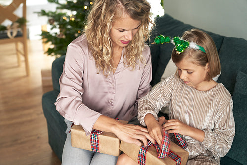 Caucasian girl and mother packing Christmas present  on sofa