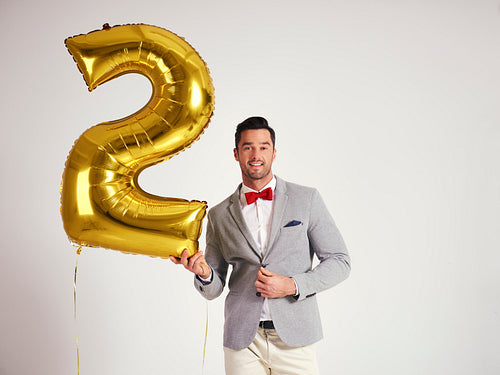 Young man with golden balloon celebrating second birthday his company