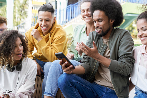Group of smiling young friends sitting together with mobile phone